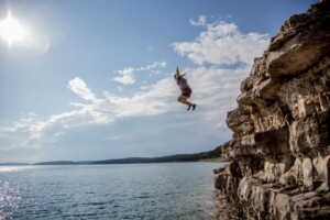 A person is jumping from a rock cliff into a lake