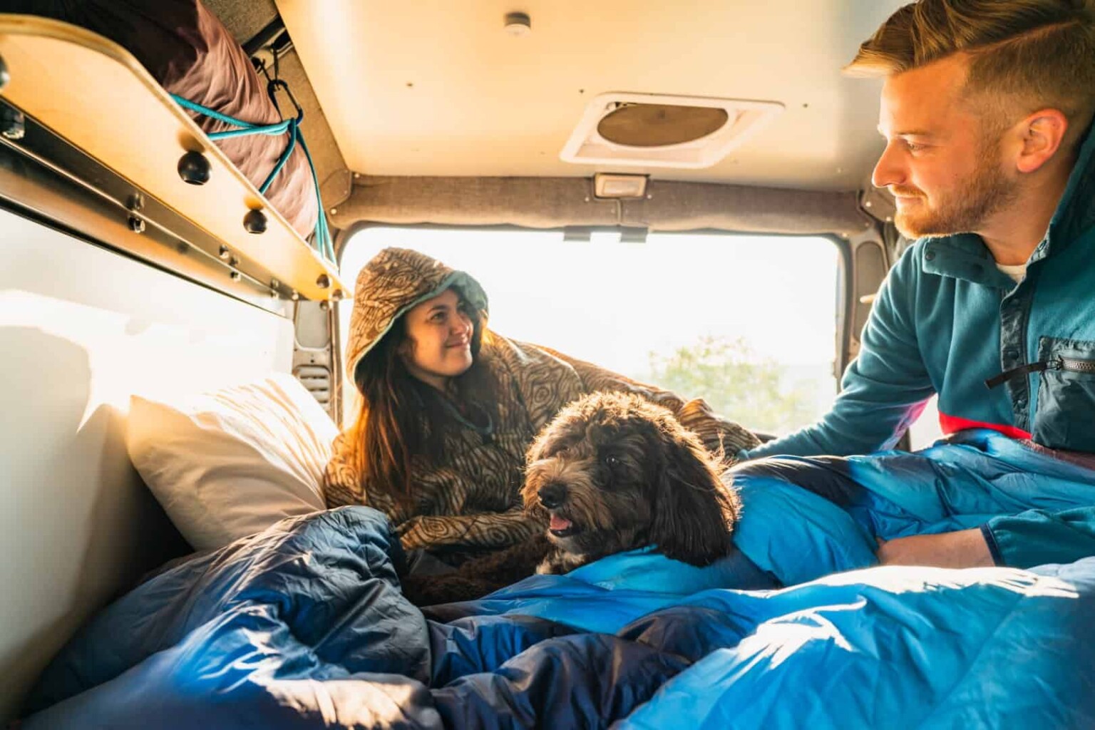 Photo of couple lounging in van with dog enjoying camper van life
