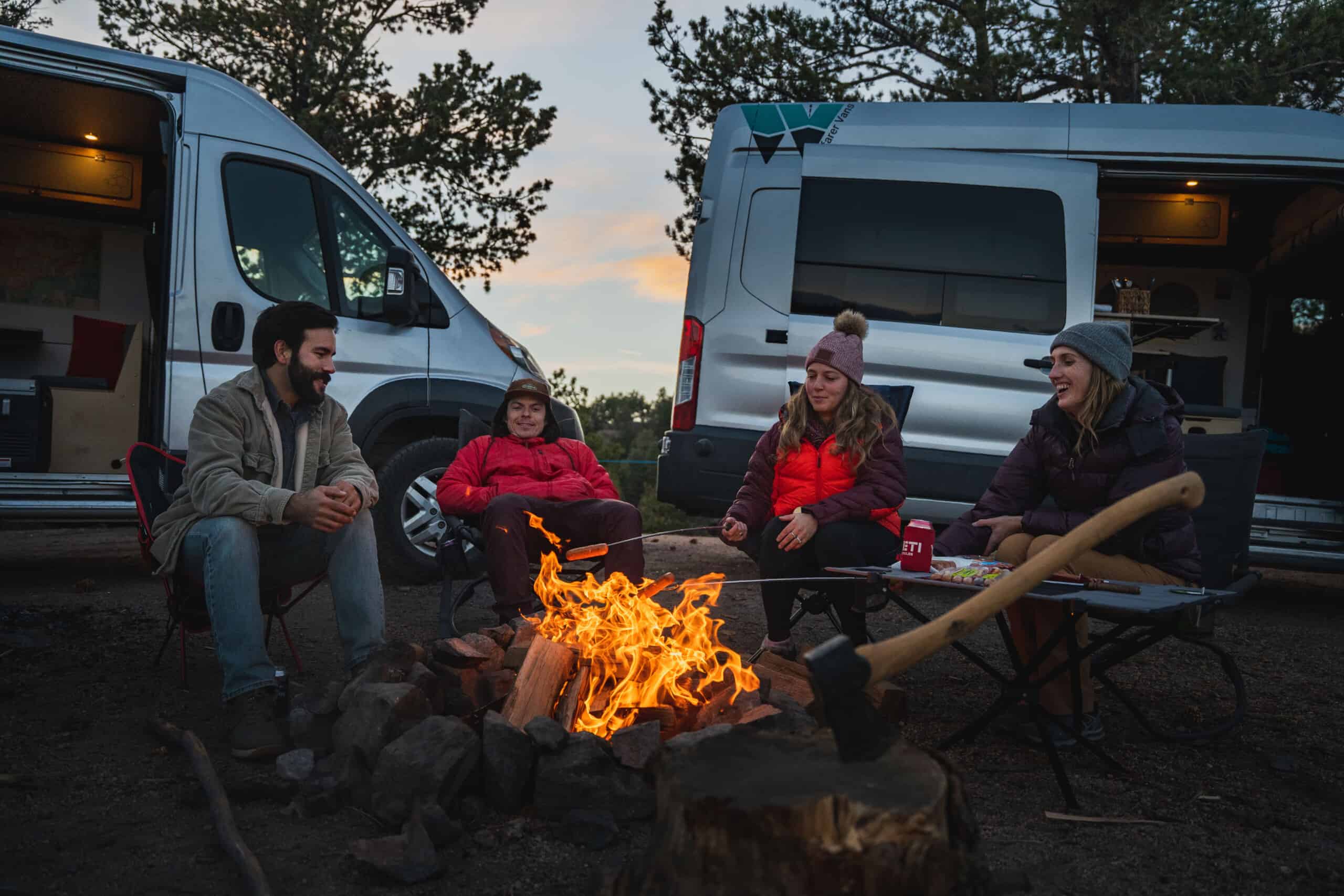 friends around a camp fire with camper van conversions in the background