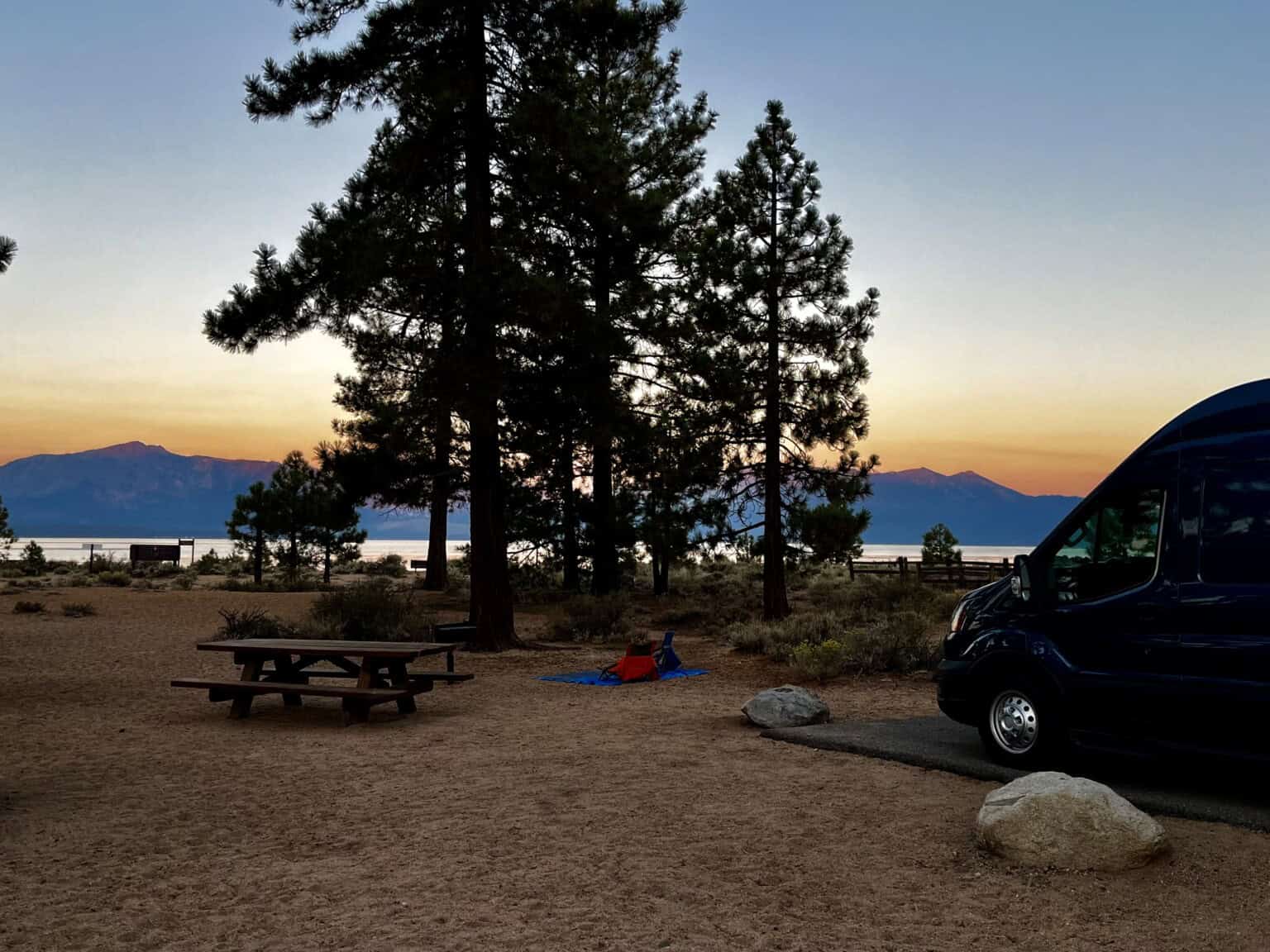 Multicolored sunset behind a camper van with pine trees in the foreground