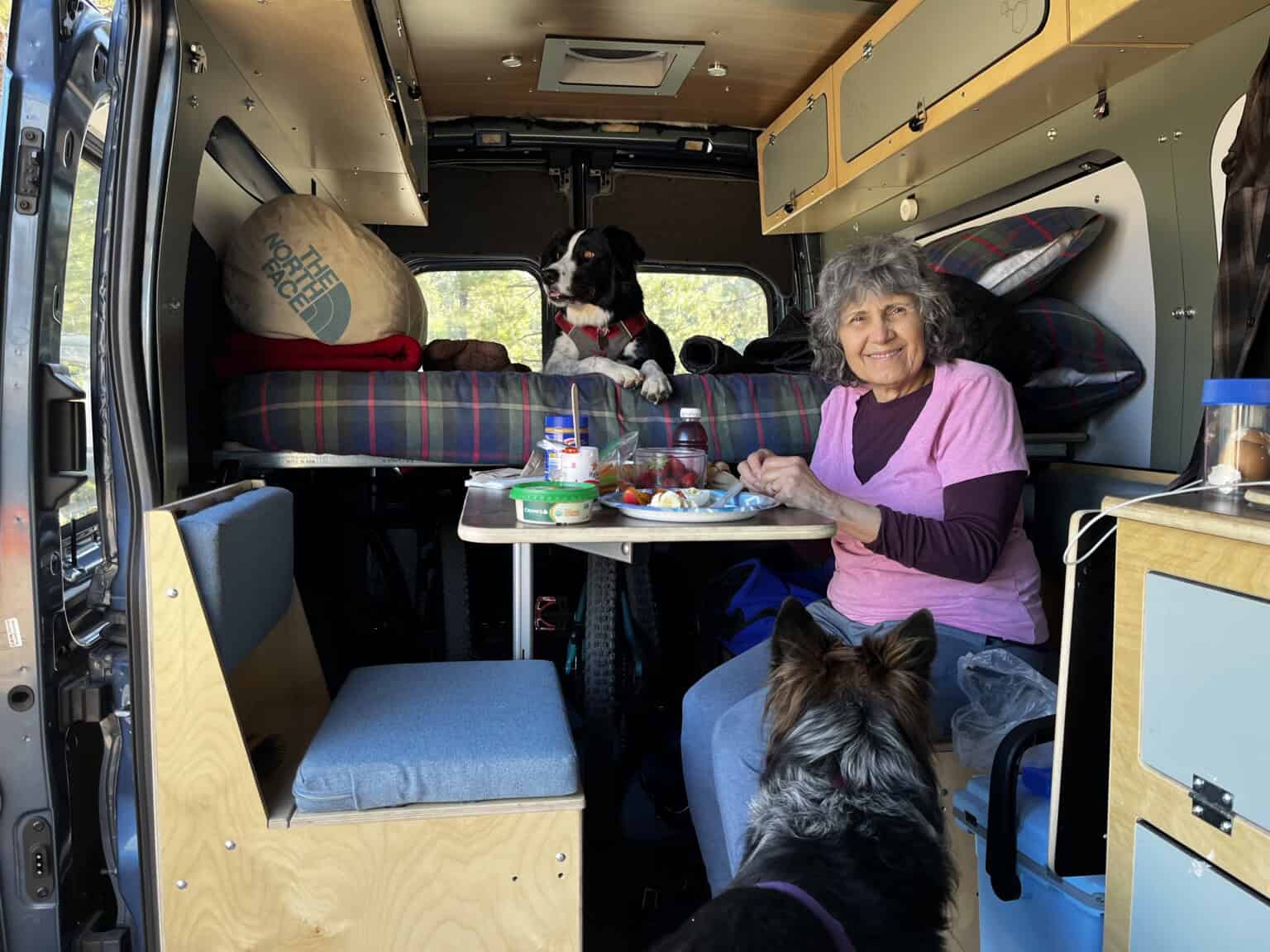 A woman sitting and smiling inside a camper van with her two dogs.