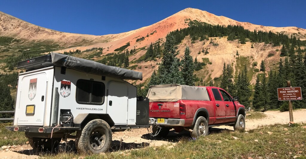 a pull behind trailer being towed by a pick up truck in front of a mountain sign