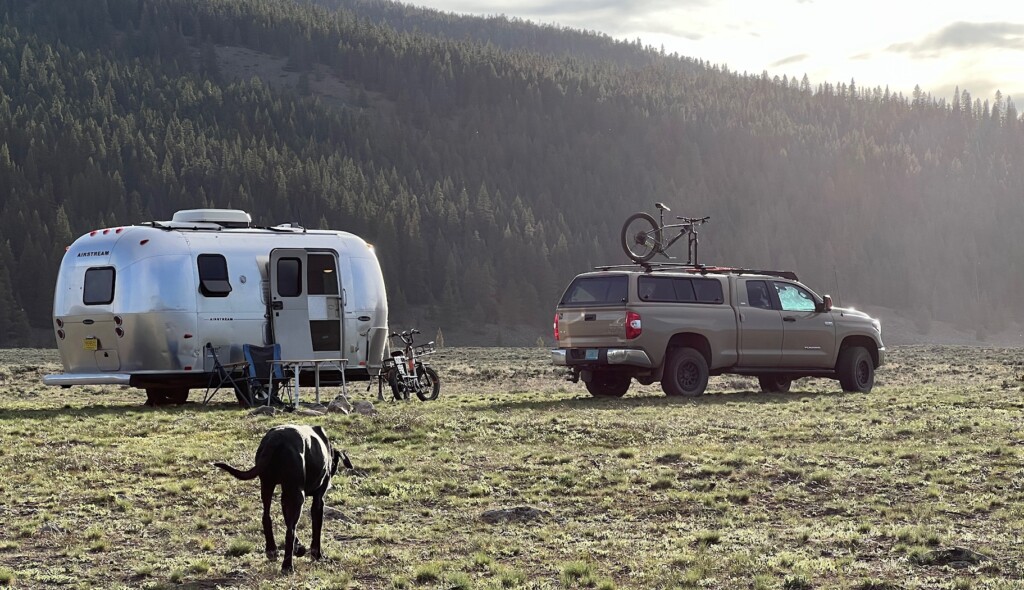 outside with a trailer, a pick up truck with a bike on the roof, and a dog